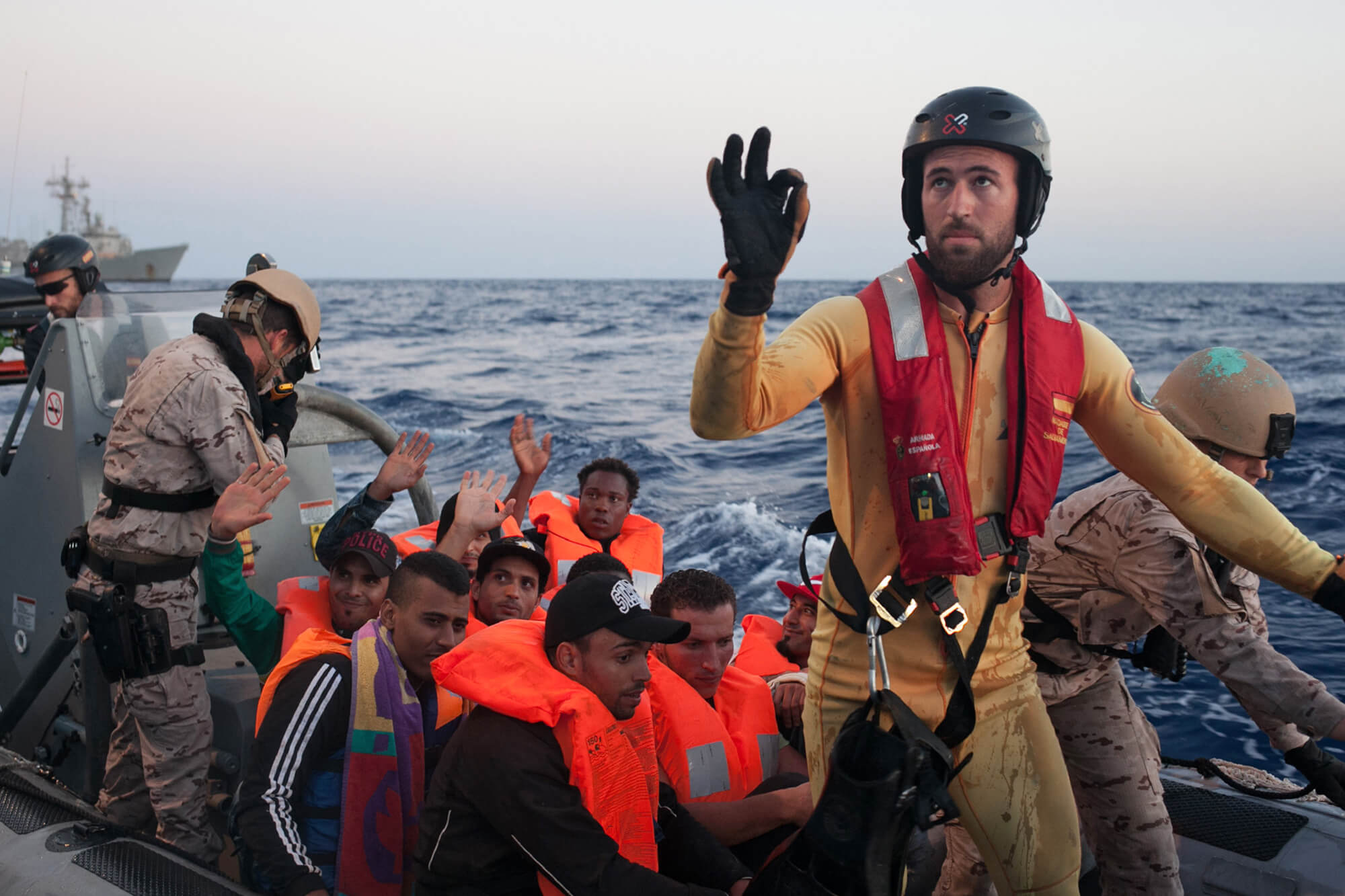 A person from the other rescue team show a perfect symbol with high handy. In the background the rescued migrants and some other people are on the RHIB.